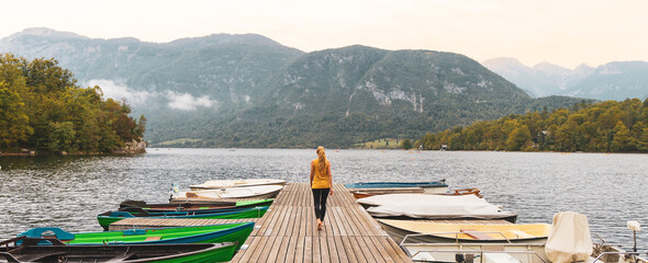 Woman tourist walking on pier with boats on Bohinj lake in Slovenia- travel,vacation,tour tourism