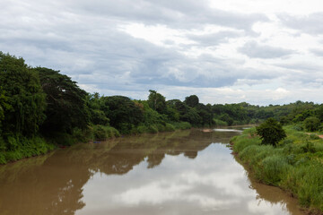 North Thailand River Landscape. Muddy river flowing through green fields in bushes in North Thailand.