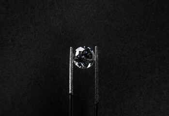 Obraz premium macro view from above of a diamond gripped with tweezers on black background