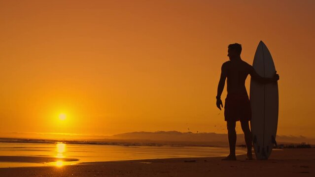 Silhouette of surfer on shore at sunset