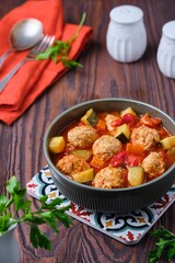 Albondigas, soup or stew, meatballs with vegetables in tomato sauce in a ceramic bowl on a brown wooden background.