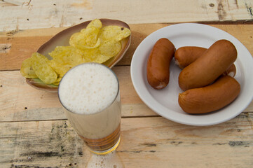 Beer in a glass with foam, sausages, chips on boards in the garden, Oktoberfest theme.