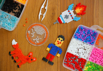 Colorful iron beads (perler or fused beads) in a box, art toys created from them and tweezers on...