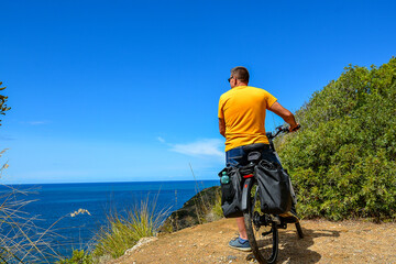 A middle-aged man wearing denim shorts and a yellow T-shirt on an electric bike stops and admires...