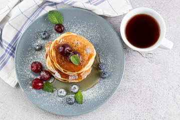 Pancakes with berries in a plate, a cup of tea on a light table. Breakfast concept.