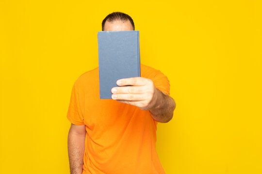 Man covering his face with the cover of a newspaper or book, isolated on yellow background.