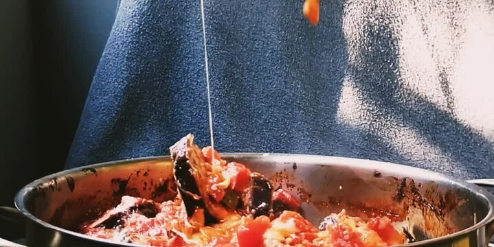 The women hand opens the lid of the pan and applies a portion of eggplant parmigiana with a spatula.