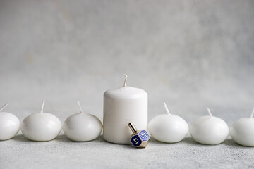 Ivory colored scented candles with blue Hanukkah dreidel placed on concrete background