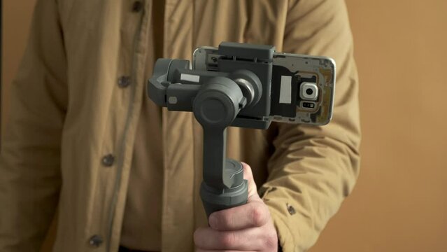 Man filming with a smartphone using a gimbal stabilizer on yellow background. Using three-axis electronic stabilizer to make vlogs or video shooting.