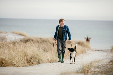 Middle aged Caucasian man walking his border collie on the beach