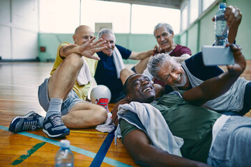 Diverse group of seniors taking a selfie on a smartphone after playing basketball in a indoor basketball gym