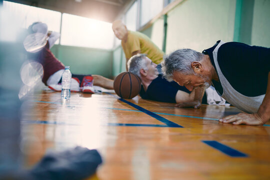 Diverse group of male seniors doing push ups and working out after playing basketball in an indoor gym - Powered by Adobe