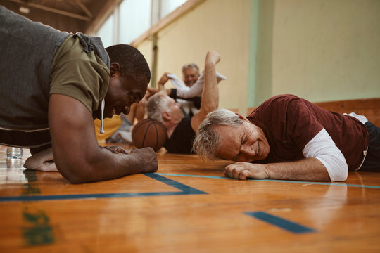 Diverse group of male seniors doing push ups and working out after playing basketball in an indoor gym - Powered by Adobe