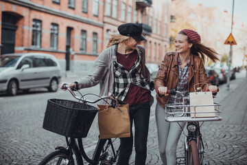 Two young female friends riding bikes while shopping in the city