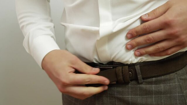 The man fastens the belt on his pants. Stylish men's accessory.