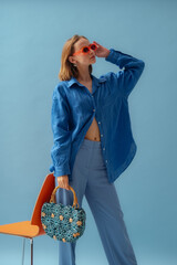 Fashionable young woman wearing trendy orange sunglasses, oversized blue linen shirt, trousers,...