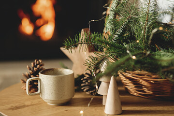 Cozy winter. Stylish cup of warm tea, basket with fir branches, wooden trees and star, pine cones...
