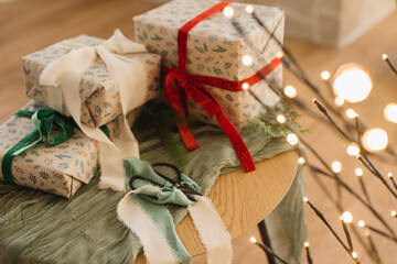 Merry Christmas and Happy Holidays! Stylish wrapped christmas gifts with ribbons and scissors on table with festive golden lights. Modern presents, atmospheric christmas eve