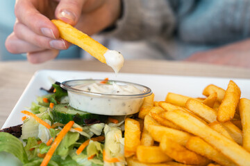 Woman hand dipping delicious French fries into mayonnaise sauce, cheese sauce. Hand hold a french...