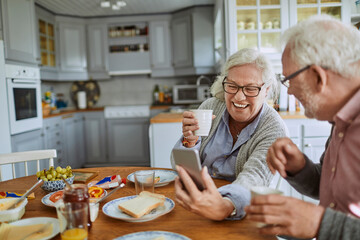 Senior Caucasian couple using a smartphone while having breakfast together in the kitchen in the morning