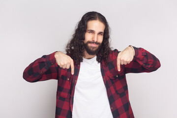 Portrait of bossy anger bearded man with long curly hair in checkered red shirt pointing down and...