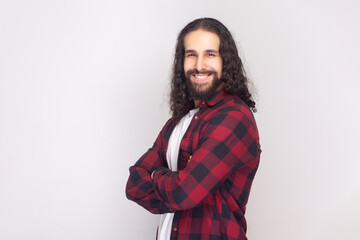 Side view portrait of smiling happy bearded man with long curly hair in checkered red shirt...