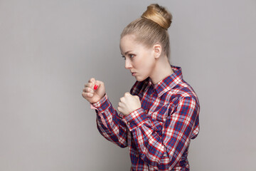 Side view portrait of angry woman with bun hairstyle standing with clenched fists, being ready to...