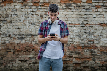 One young men a teenager with headphones standing in front of brick wall with mobile phone