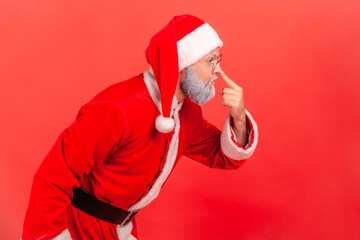 Side view portrait of elderly man with gray beard wearing santa claus costume touching nose with...
