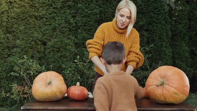mom and son carve Halloween pumpkin on backyard table