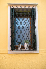 A window with green wooden shutters and a yellow wall. Italy