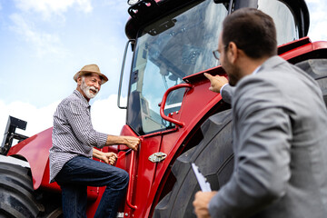 Farmer entering new tractor machine while professional seller presenting new features to the buyer. Investing in agricultural machinery.