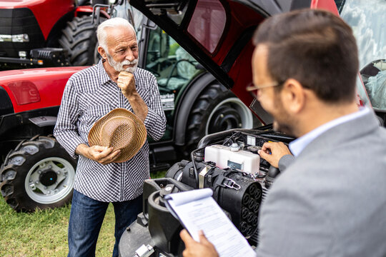 Professional tractor seller presenting new agricultural machine to the farmer. Showing features and engine of tractor machine.