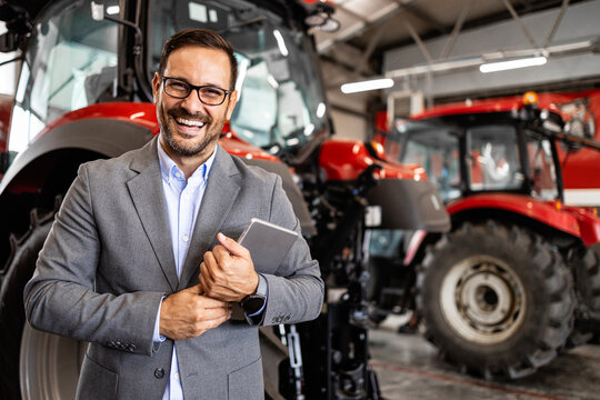 Tractor salesman standing in workshop providing service and regular maintenance for agricultural machinery.
