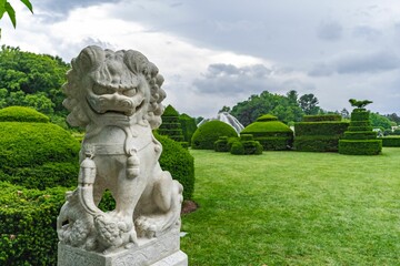 Chinese guardian lion statue in a lush garden, surrounded by vibrant green foliage