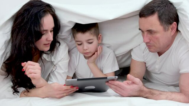 banner. latest technology family husband wife and child sitting watching movie on laptop on bed relaxing together white cloth.es chatting online relatives mom dad and son laughing smiling rejoicing