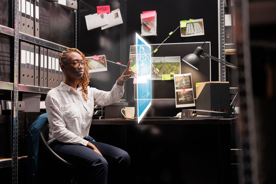 Female investigator looking at evidence hologram, examining artificial intelligence image to solve felony in archive room. Private detective working with augmented reality clues.