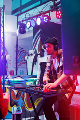 Dj mixing electronic music on digital controller at party in nightlife. Young man musician in headphones performing with mixer console panel on stage with spotlights at concert in club