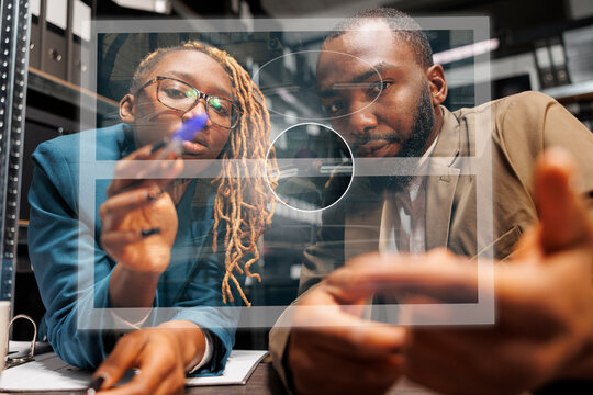 Young detectives checking hologram in incident room, examining artificial intelligence holographic image. Two inspectors working with augmented reality, looking at clue photos.