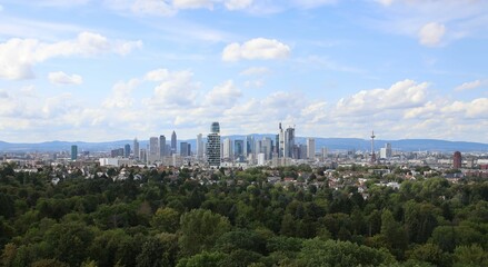 Panoramic view of the Frankfurt skyline with green forest in the foreground on a sunny day.