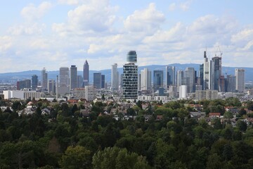 Obraz premium Panoramic view of the Frankfurt skyline with green forest in the foreground on a sunny day.