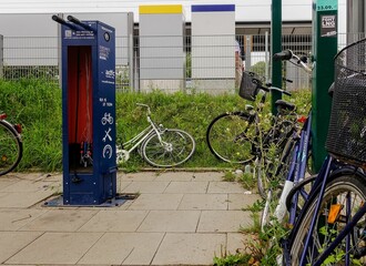 Telephone booth stands adjacent to a tall white building, with several bicycles parked nearby - Powered by Adobe