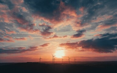 Picturesque view of a windmill farm atop a hill with the sun setting in the background