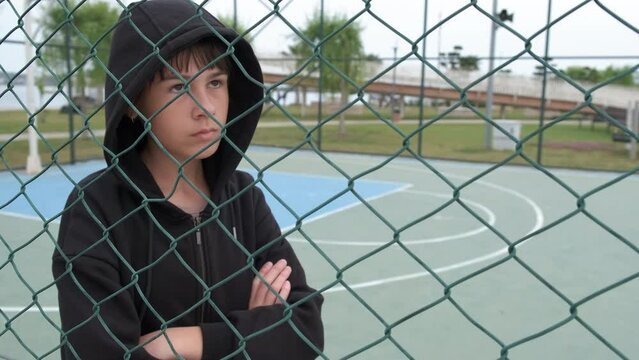 Poverty emotions by metal fence. A young gilr in poverty stay with sad emotions by fence on playground.