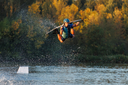An athlete jumps from a springboard. Wakeboard park at sunset. A man performs a trick on a board