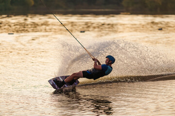 An athlete performs a trick on the water. Park at sunset. Wakeboard rider