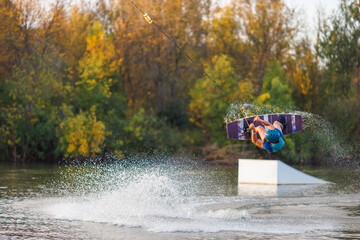 An athlete jumps from a springboard. Wakeboard park at sunset. A man performs a trick on a board