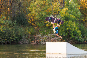 An athlete jumps from a springboard. Wakeboard park at sunset. A man performs a trick on a board