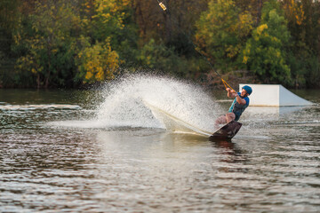 An athlete performs a trick on the water. Park at sunset. Wakeboard rider