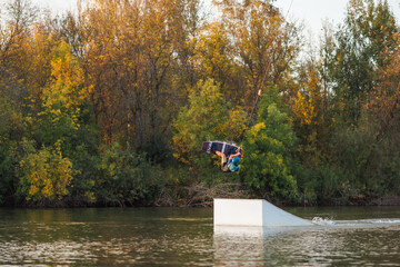 An athlete jumps from a springboard. Wakeboard park at sunset. A man performs a trick on a board